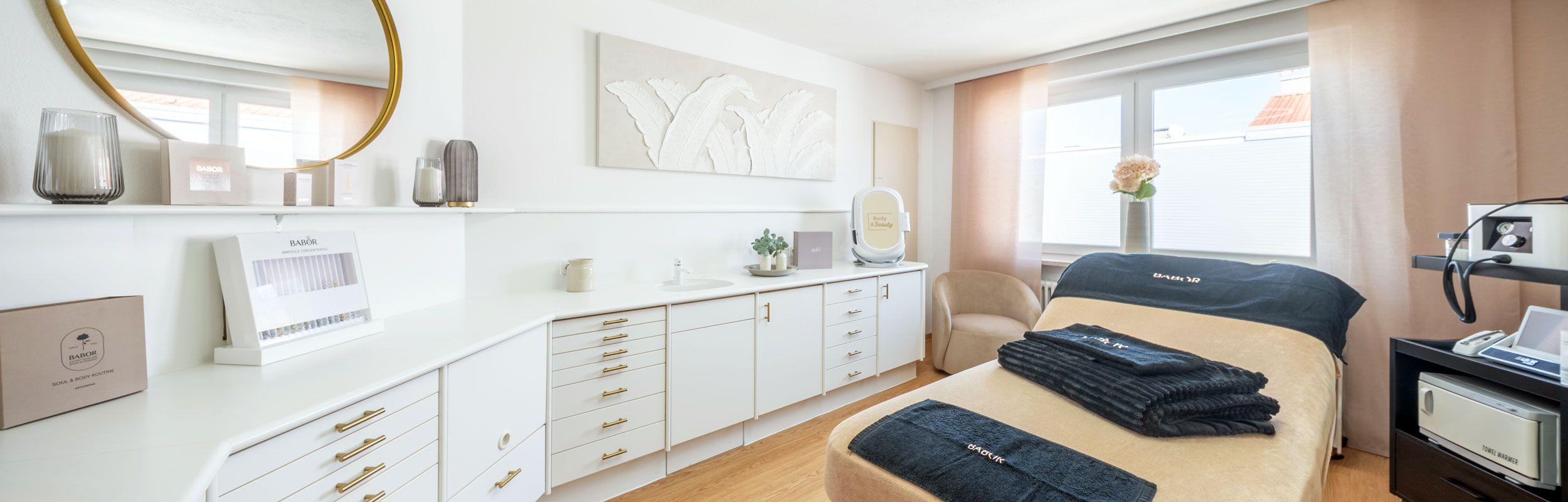 Behandlungsraum von BODY & Beauty mit Liege, Spiegel und Pflegeschrank